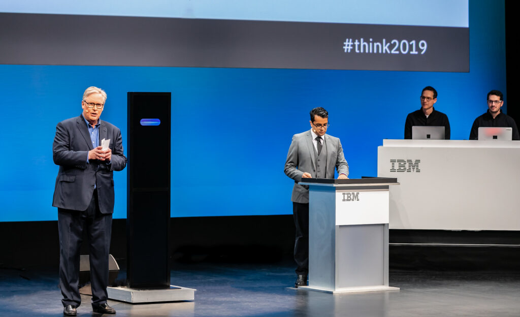 John donvan e harish natarajan sobre palco, junto a ia da ibm