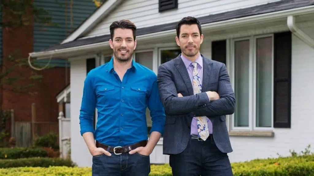 Jonathan e drew scott posam em frente a uma casa no irmãos à obra, programa do discovery h&h