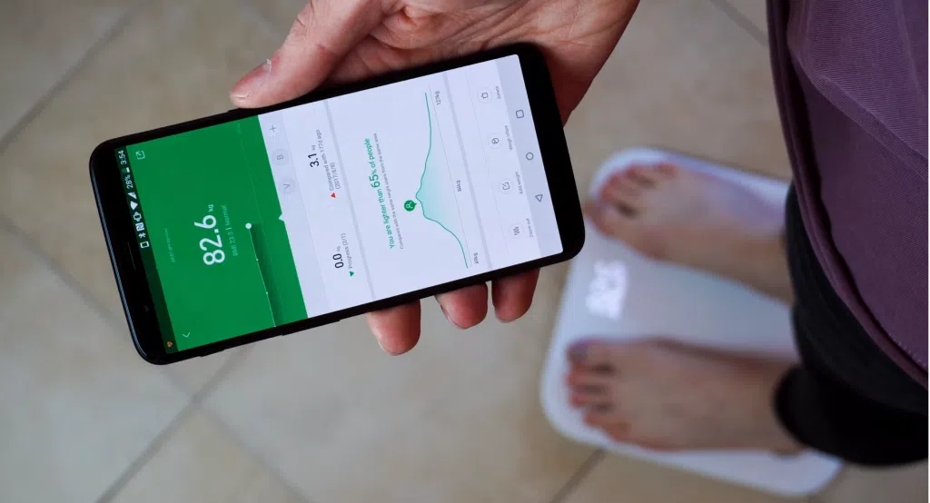Balança inteligente ligada ao aplicativo no celular, mostrando dados sobre o peso do usuário.