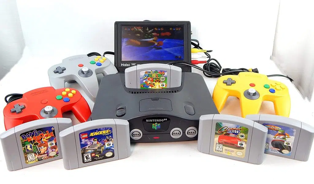 O nintendo 64 com diversas fitas e um periférico de tv acoplado a ele.