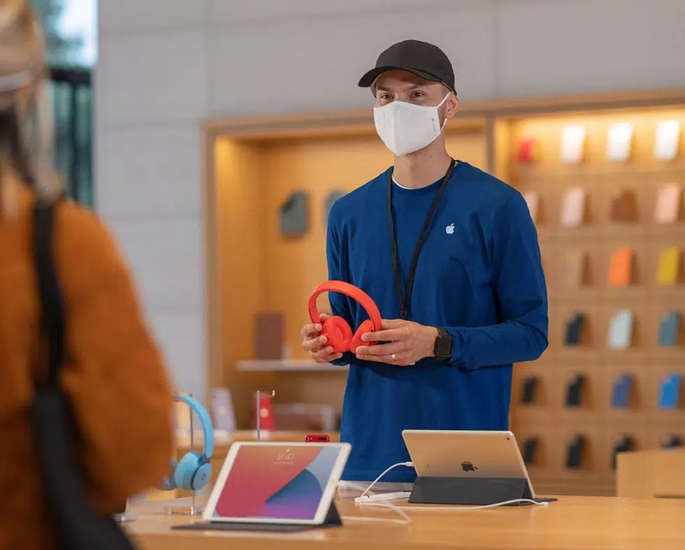 Funcionário de uma loja física da apple com camisa azul, realizando uso de máscara