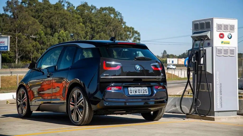 Imagem de uma bmw estacionada ao lado de uma estação de carregamento para veículos elétricos.