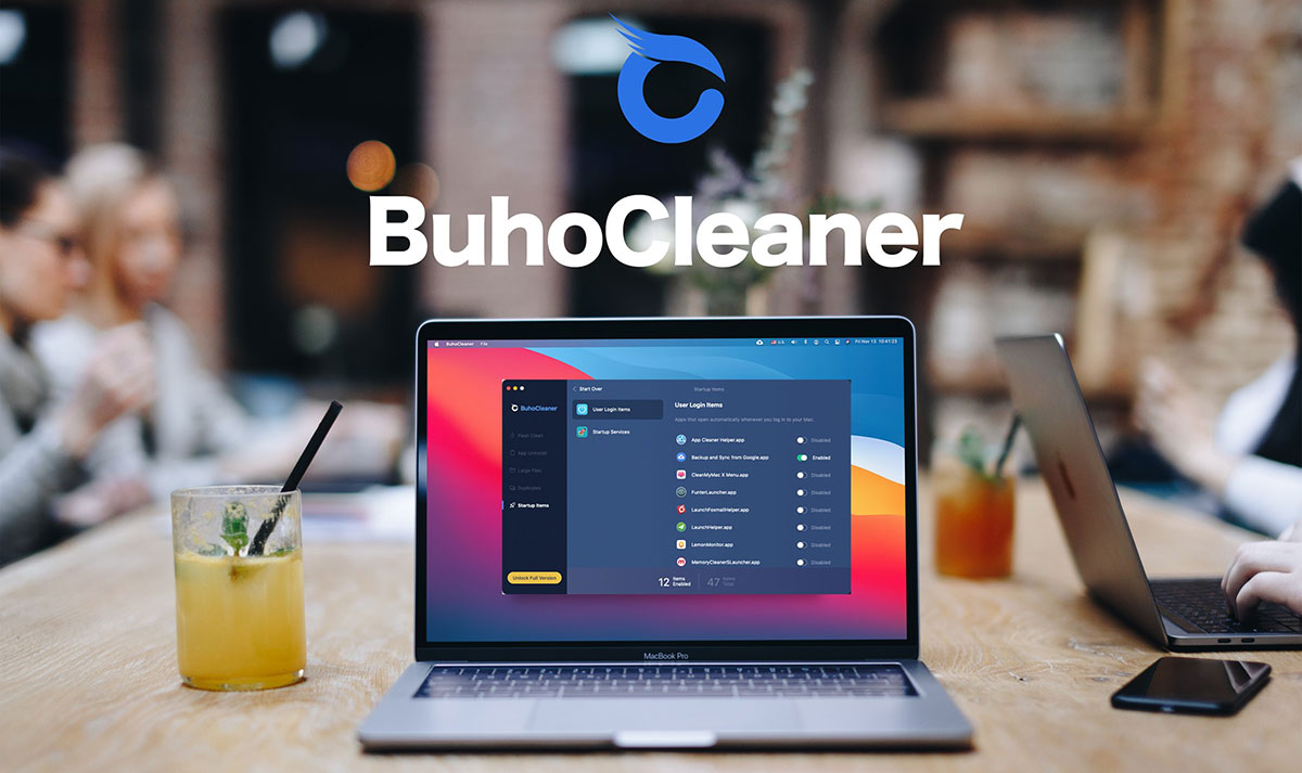 Macbook com buhocleaner aberto, em cima de uma mesa ao lado de outros laptops e um copo de suco