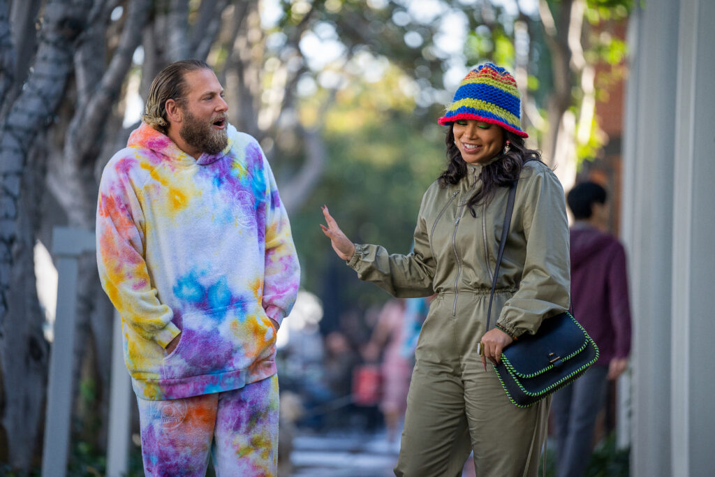 Equipe de certas pessoas da netflix em foco, na esquerda homem com casaco pintado a mão e na direita mulher com sobretudo verde-claro.