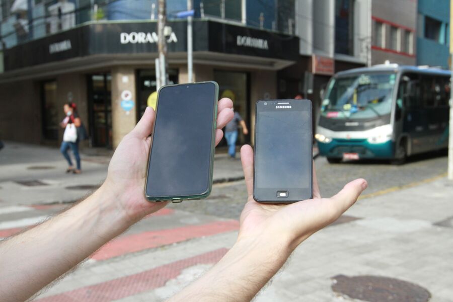 Pessoa segurando dois smartphones no meio de uma avenida movimentada com carros