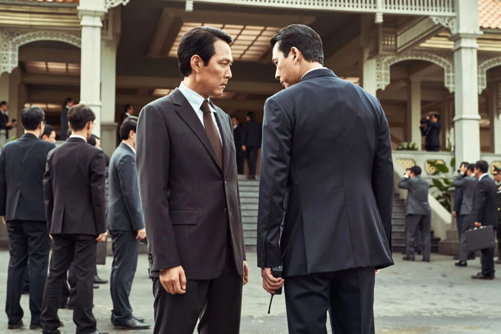 Filme "operação hunt", dirigido por lee jung-jae, estará em cartaz no brasil em fevereiro. A imagem mostra o ator de terno durante cena de espionagem, conversando com outro personagem.