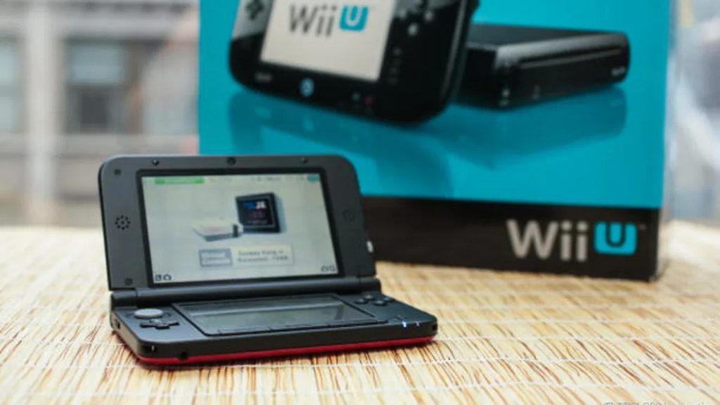 Foto de um nintendo 3ds com uma caixa do console nintendo wii u ao fundo