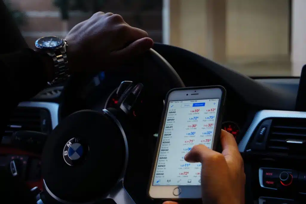 Homem no carro fazendo trading no celular.