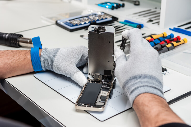 Lixo eletrônico t alt | celular aberto na sua estrutura, com mãos usando luvas cinzas inspecionando o objeto