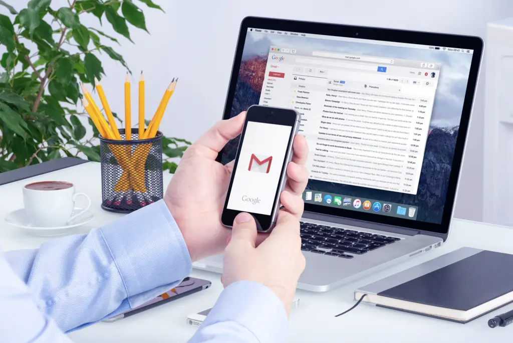 Aplicativo gmail na tela do iphone em mãos de homens e versão desktop do gmail na tela do macbook. O gmail é um serviço de e-mail gratuito fornecido pelo google. Todos os gadgets em foco.